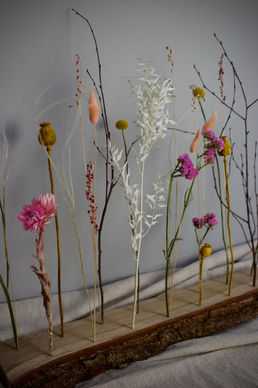 Blütenleiste ‚Frühlingserwachen‘ - DIY Set. Trockenblumen in Pink, Gelb und Weiß treffen auf naturbelassenes Eichenholz mit markanter Rinde.