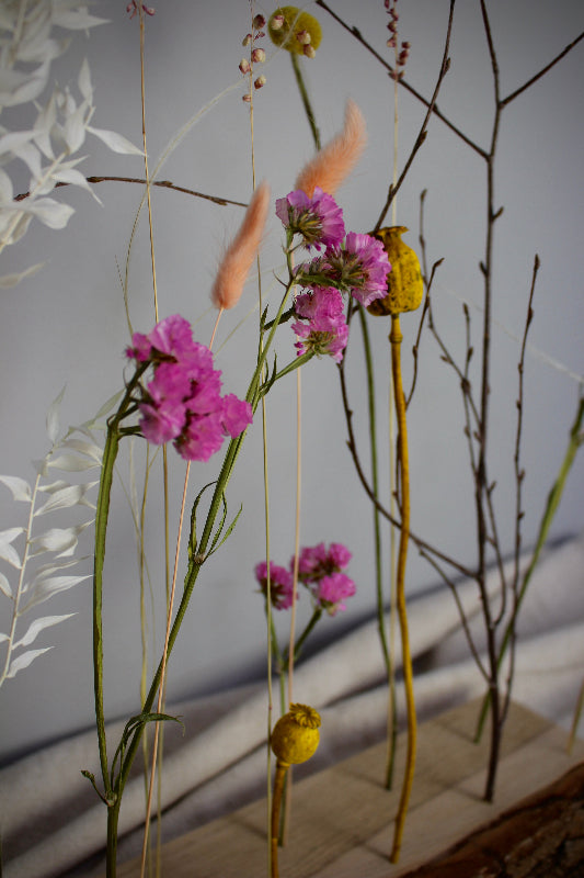 Blütenleiste ‚Frühlingserwachen‘ - DIY Set. Trockenblumen in Pink, Gelb und Weiß treffen auf naturbelassenes Eichenholz mit markanter Rinde.